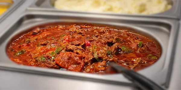 Greek chicken stifado in tomato and red wine sauce served in a foodservice tray.