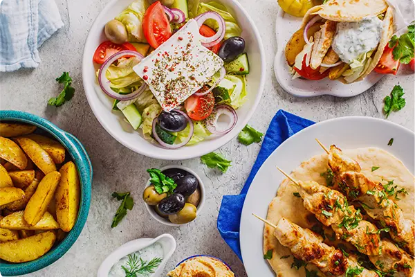 Mediterranean food spread with Greek salad, grilled chicken skewers, pita, potatoes and tzatziki sauce