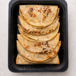 Black Bean and Corn Quesadillas stacked in a black foodservice tray, pre-grilled and shipped frozen, 18 per case