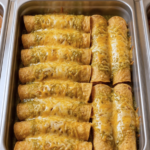 Baked vegetable enchiladas with salsa verde and melted cheddar cheese in a steam table pan for foodservice by Demeter's Pantry