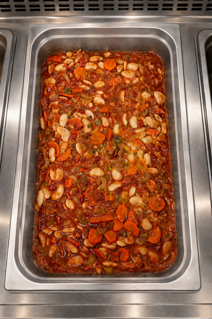 Demeter's Pantry Greek white bean stew with fire roasted tomatoes, carrots, and celery in a hot bar tray