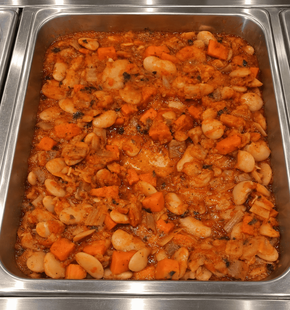 Close-up of a hearty bean and vegetable stew in a stainless steel tray. Demeter's Pantry Mediterranean White Bean Stew in Hot Bar Pan
